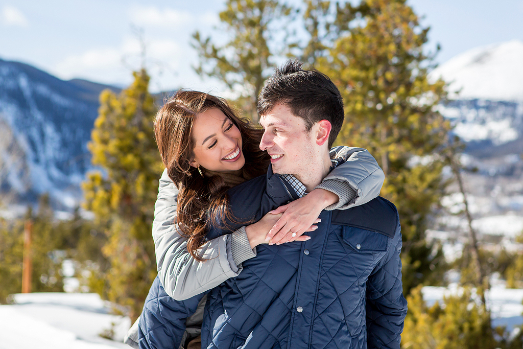 Scott and Stephanie smiling at each other in front of pine trees on a trail near Lake Dillon CO.