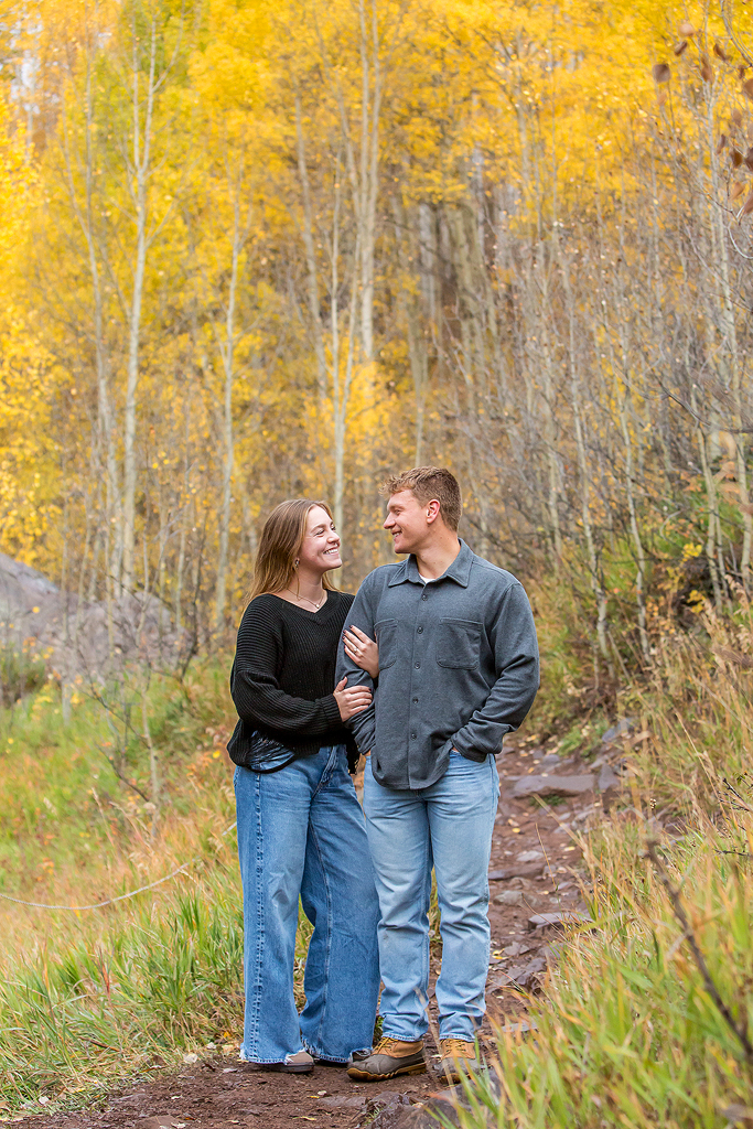 Claire hugs Jackson’s arm in front of changing fall colors during their Colorado engagement.