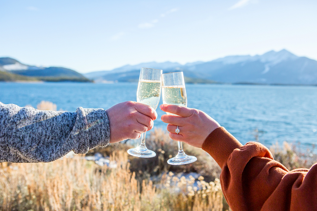 Close-up shot of two hands holding champagne flutes, one with an engagement ring.