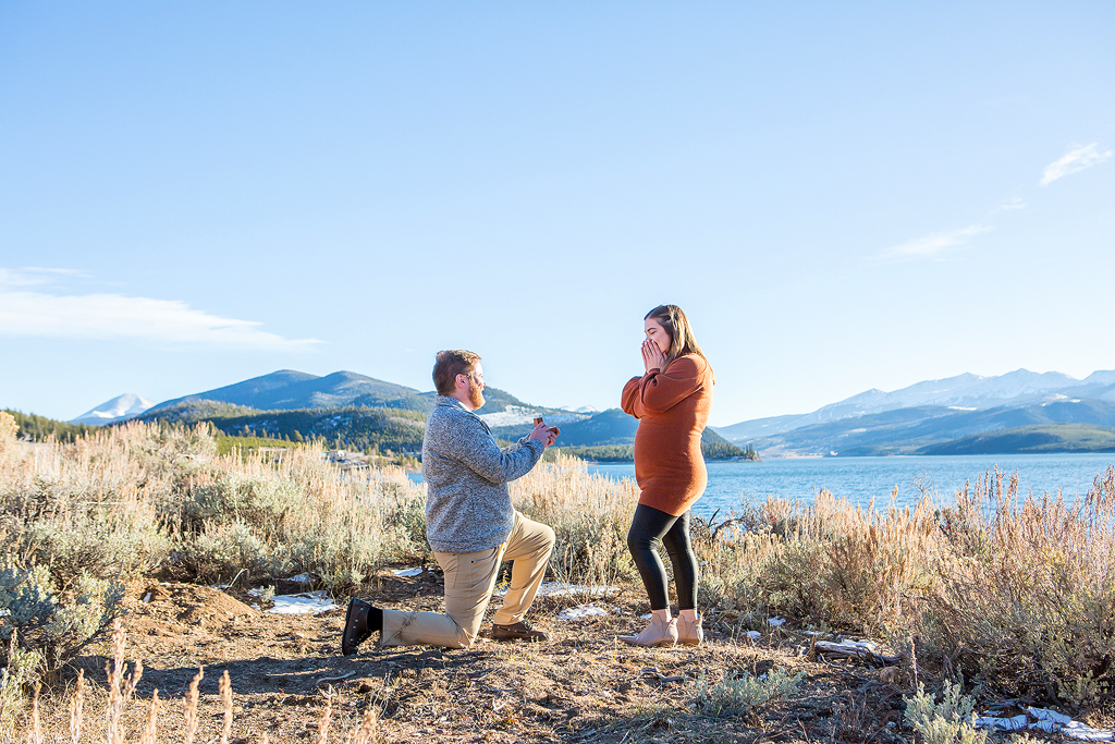 Greg kneels to propose to Rachel in front of Lake Dillon near the Dillon Marina in Colorado.