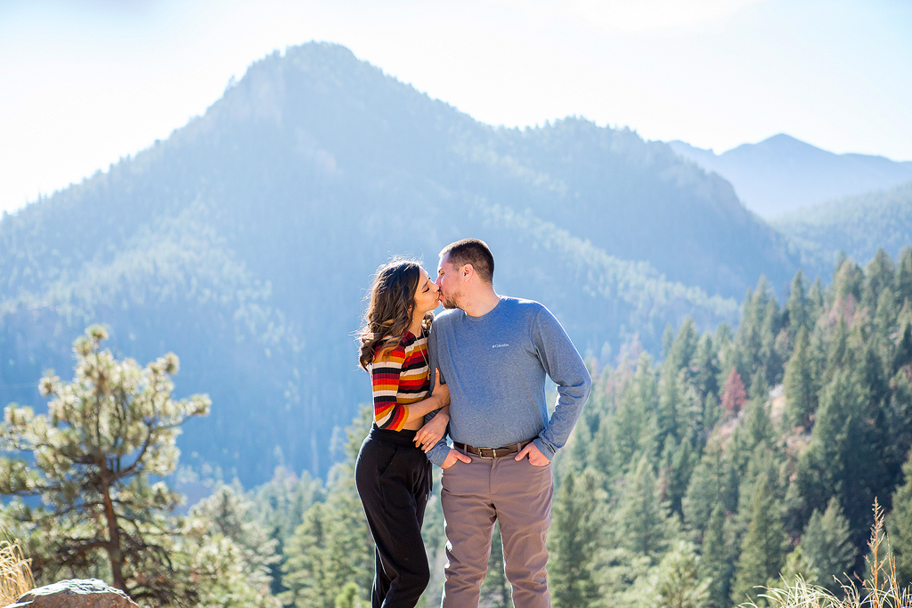 Carlos and Juliana kiss in front of a scenic overlook during their surprise proposal in Colorado.