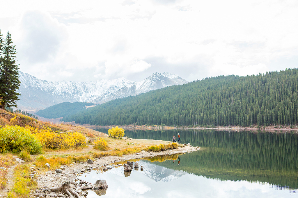 Dijon kneels to propose in front of a sweeping mountain landscape at the lake shore of Clinton Gulch.