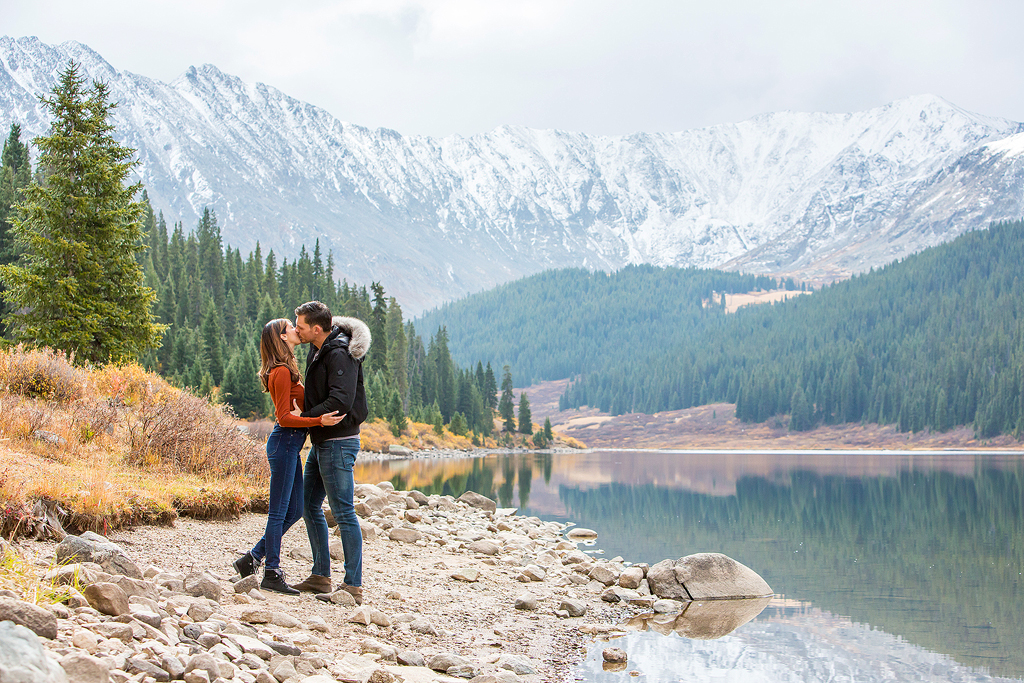 Dijon and Mana kiss with trees reflected in Clinton Gulch Reservoir behind them.