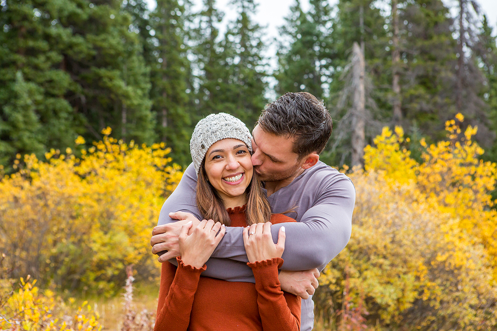 Dijon and Mana embrace in front of fall colors during their engagement in Colorado.