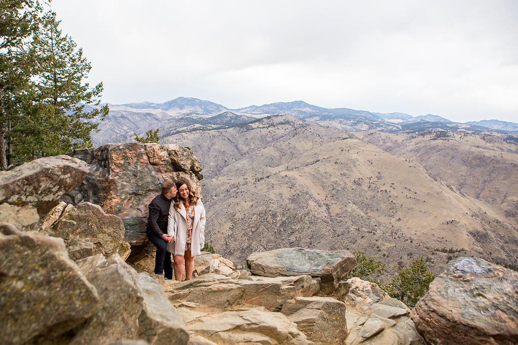 Garrett and Marissa snuggle near some rocks with a mountain view in Colorado near Golden.