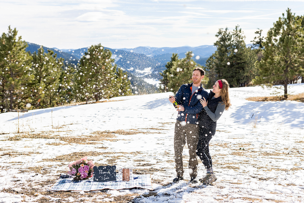 Hannah and Sam popping a bottle of champagne to celebrate their engagement in Colorado.