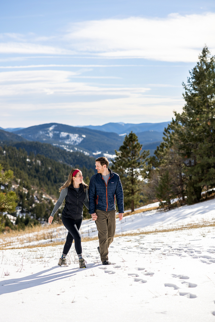 Sam and Hannah walk in a snowy meadow in Mount Falcon Park after their surprise proposal.