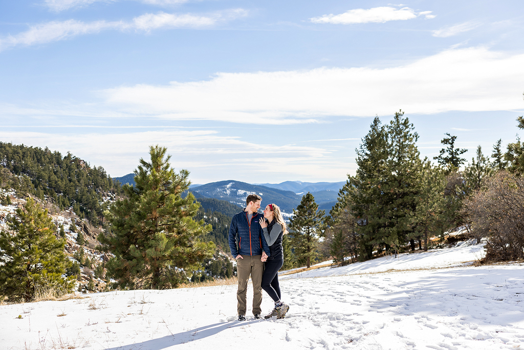 Hannah and Sam stand in a snowy field in the mountains during their engagement.