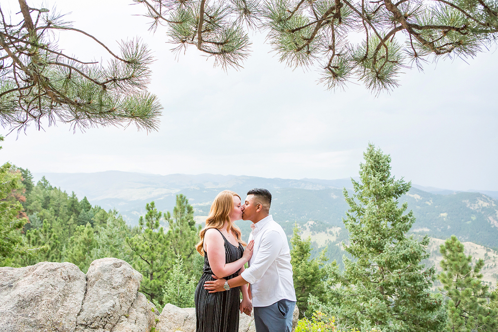 Luis and Nicole kiss in front of a scenic overlook during their proposal in Boulder, Colorado.