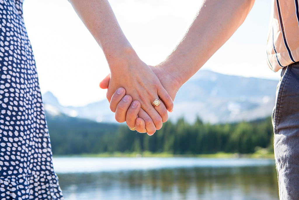 Clasped hands with an engagement ring in front of Brainard Lake in Colorado.