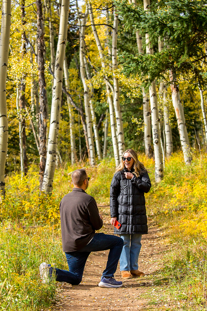 Alex huge smile of surprise as Nick proposes in a sea of vibrant yellow aspens in Colorado.