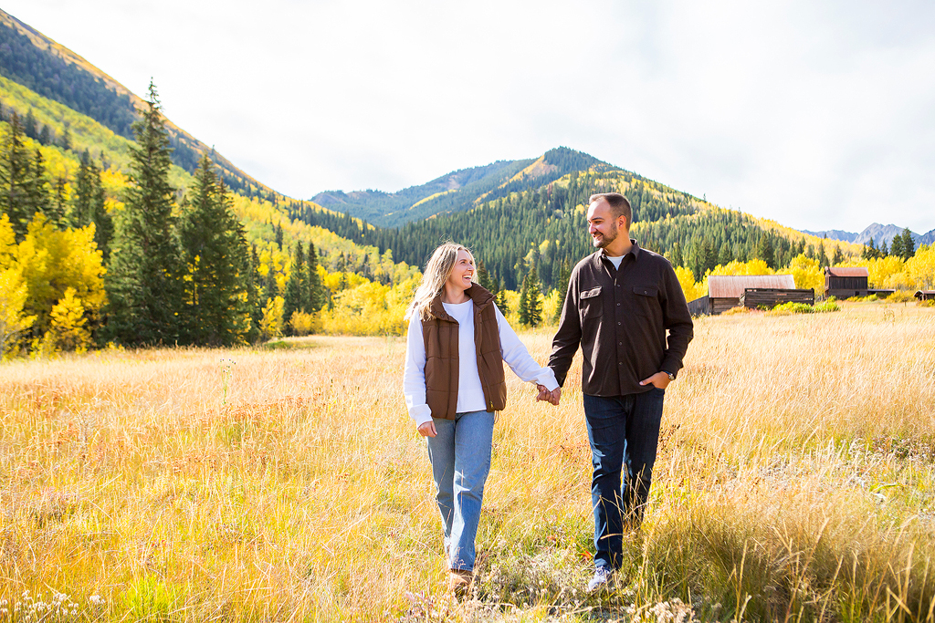Nick and Alex walk hand in hand through a meadow during the fall near Aspen, CO.