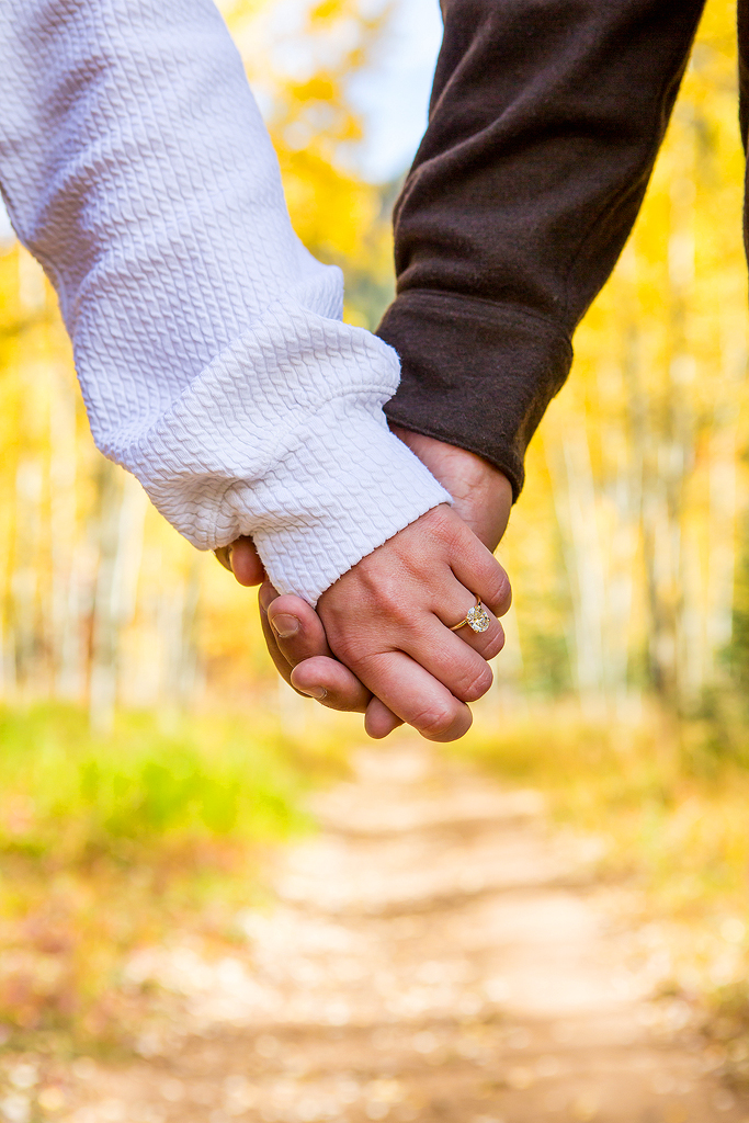 Close-up of hands with Alex’s engagement ring in front of yellow aspen leaves.