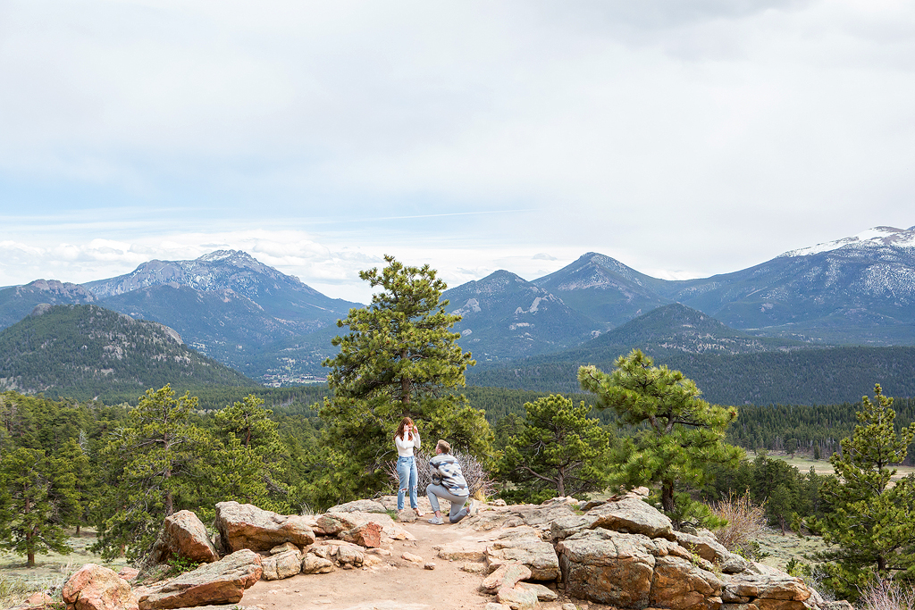 Noah kneels to propose to Lea in front of a panoramic mountain landscape at 3M Curve.