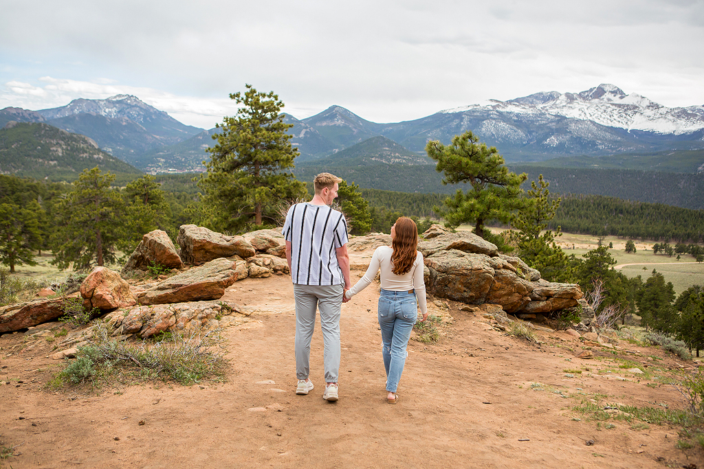 Noah and Lea hold hands with mountains behind them on a sunny spring day in Colorado.