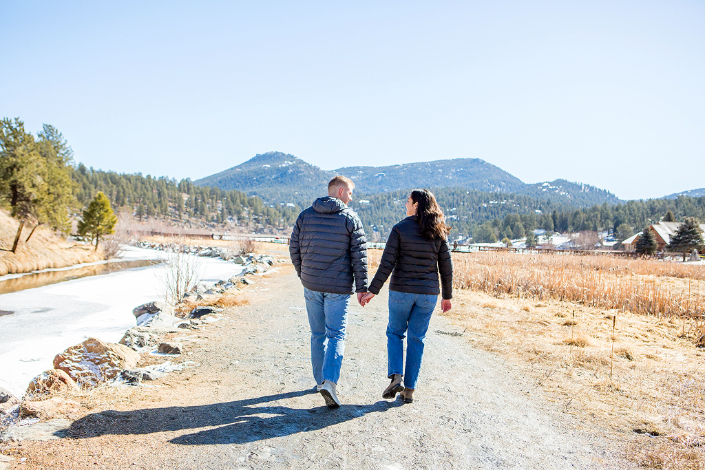 Ryan and Alissa walk with the mountains behind them after their surprise proposal at Evergreen Lake.