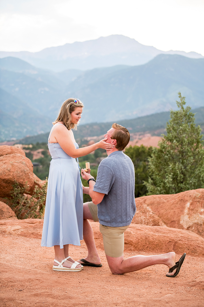 Jenna smiles softly as Stephen holds out an engagement ring in front of Colorado mountains.