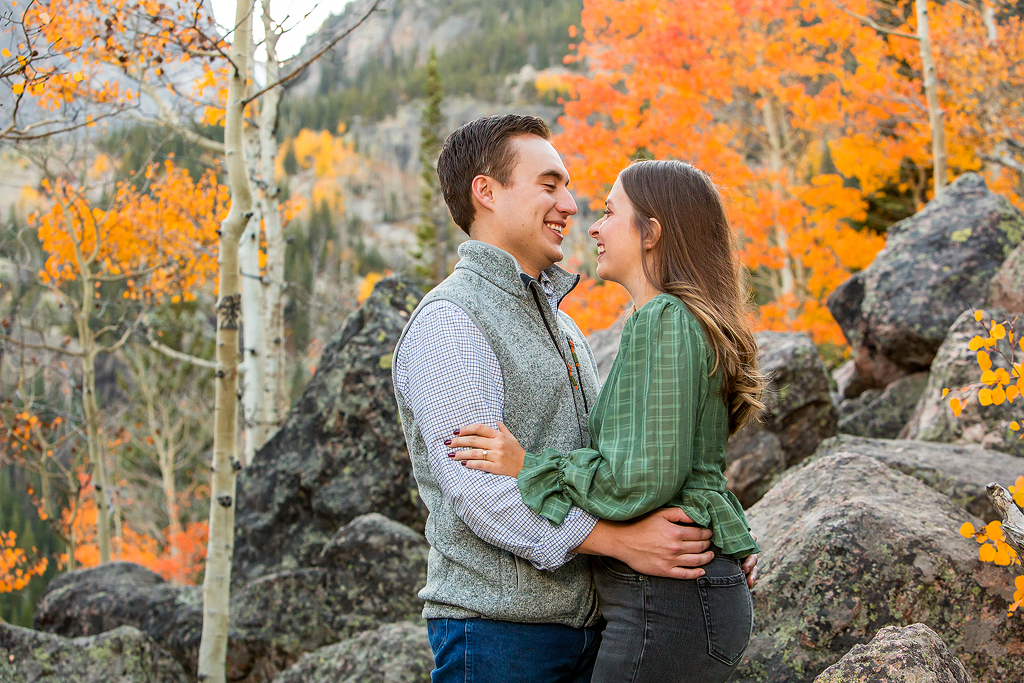 Will and Erika smile in front of aspens changing orange during the fall in Rocky Mountain National Park, CO.