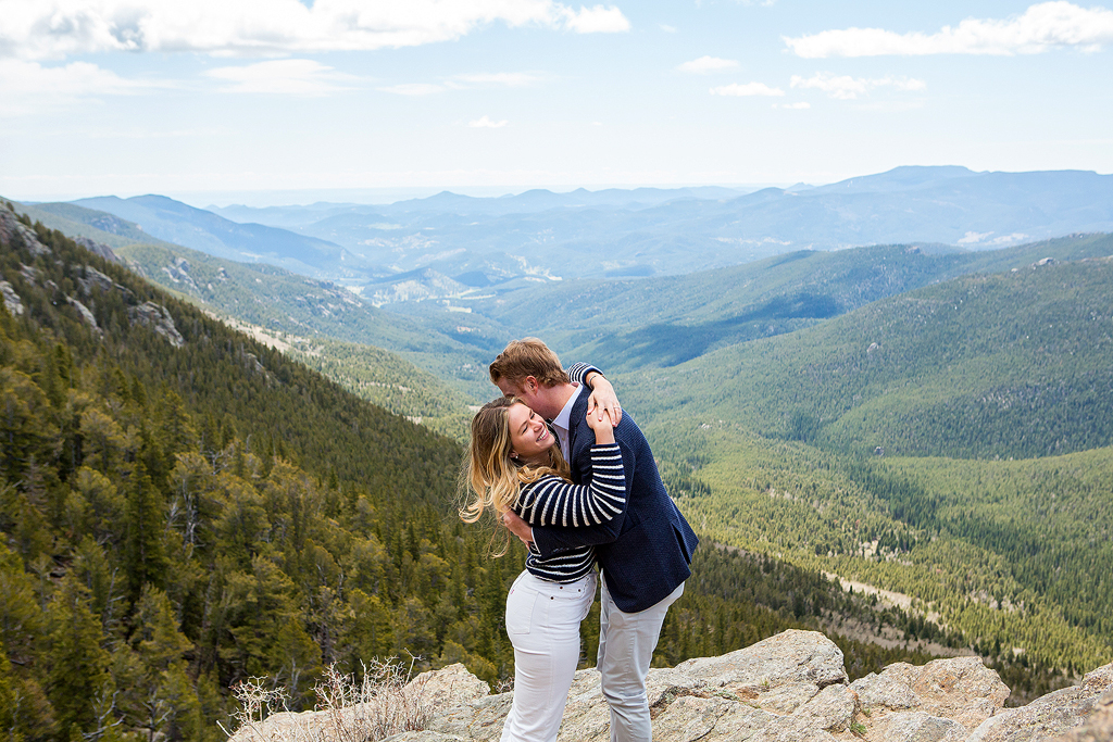 Couple hugs in front of a valley and mountain views below at Juniper Pass.