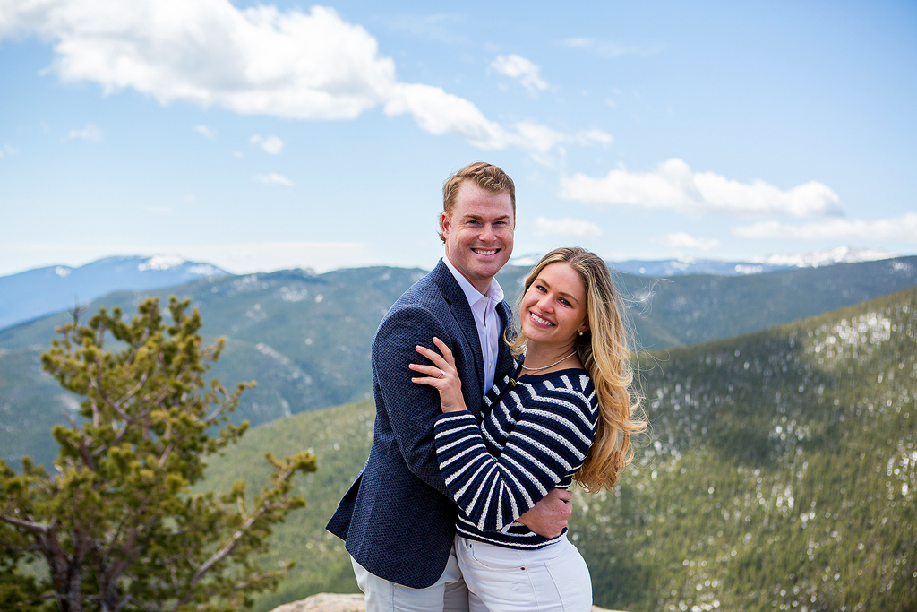 Engagement portrait of Ed and Savanah in front of pine trees and mountains.
